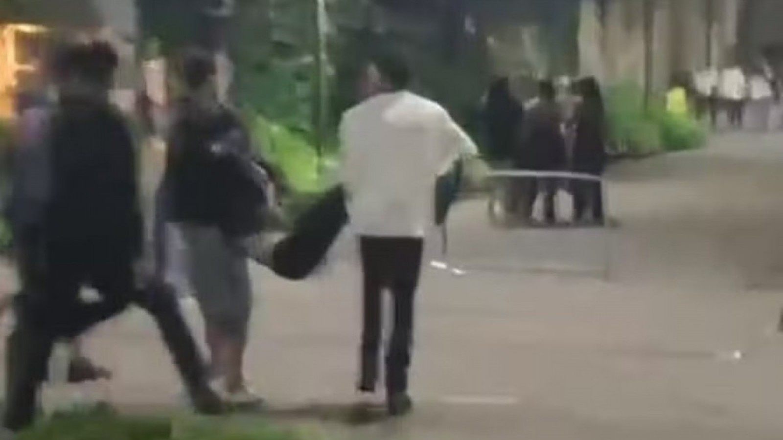 Três pessoas carregam uma figura caída em uma rua escura à noite