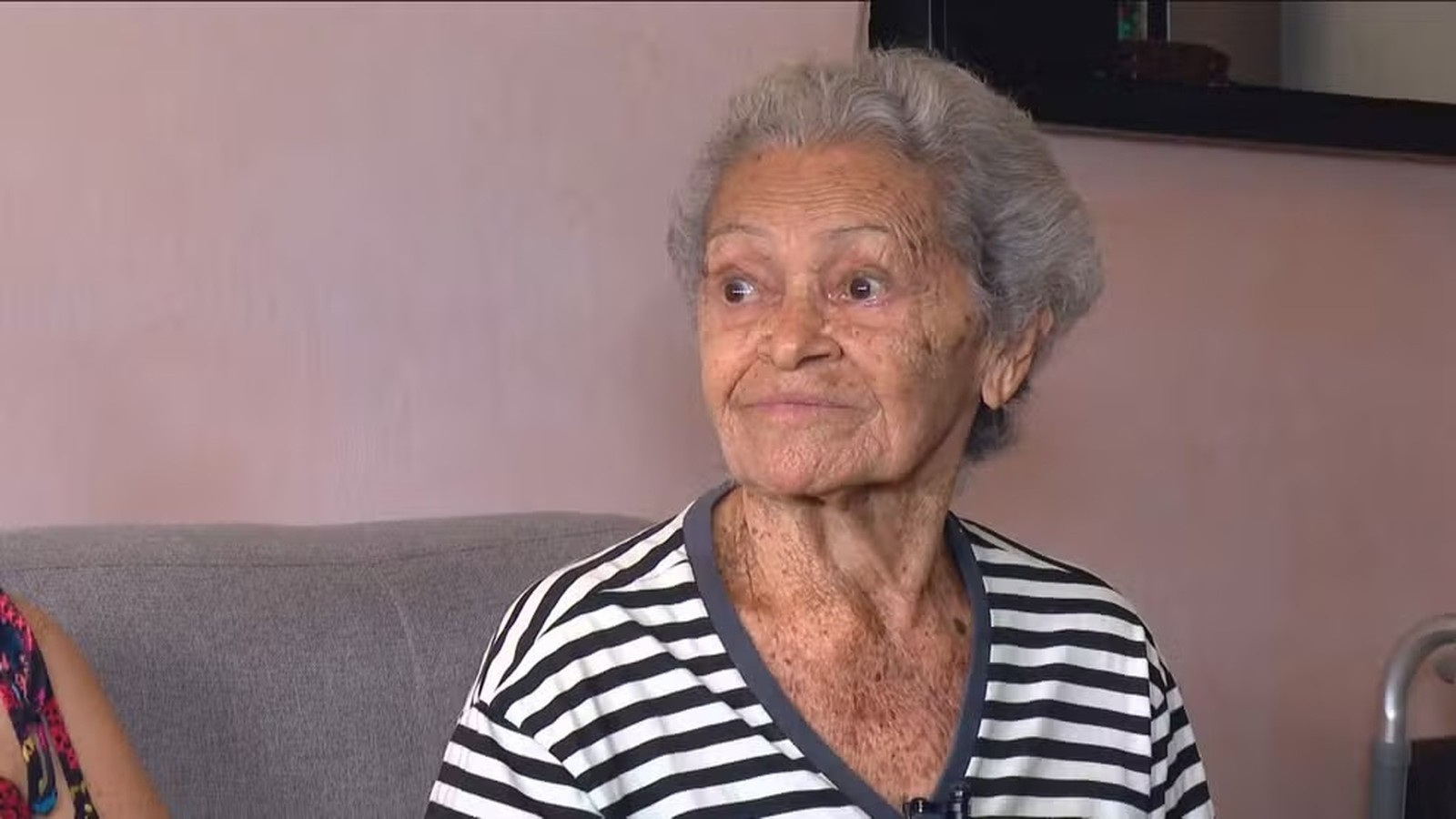 Mulher idosa de cabelos grisalhos e camisa listrada preta e branca olhando para a direita