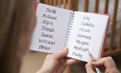 Mão segura caderno com lista de nomes de bebês: Jacob, Michael, Lily, Isabella, Emily