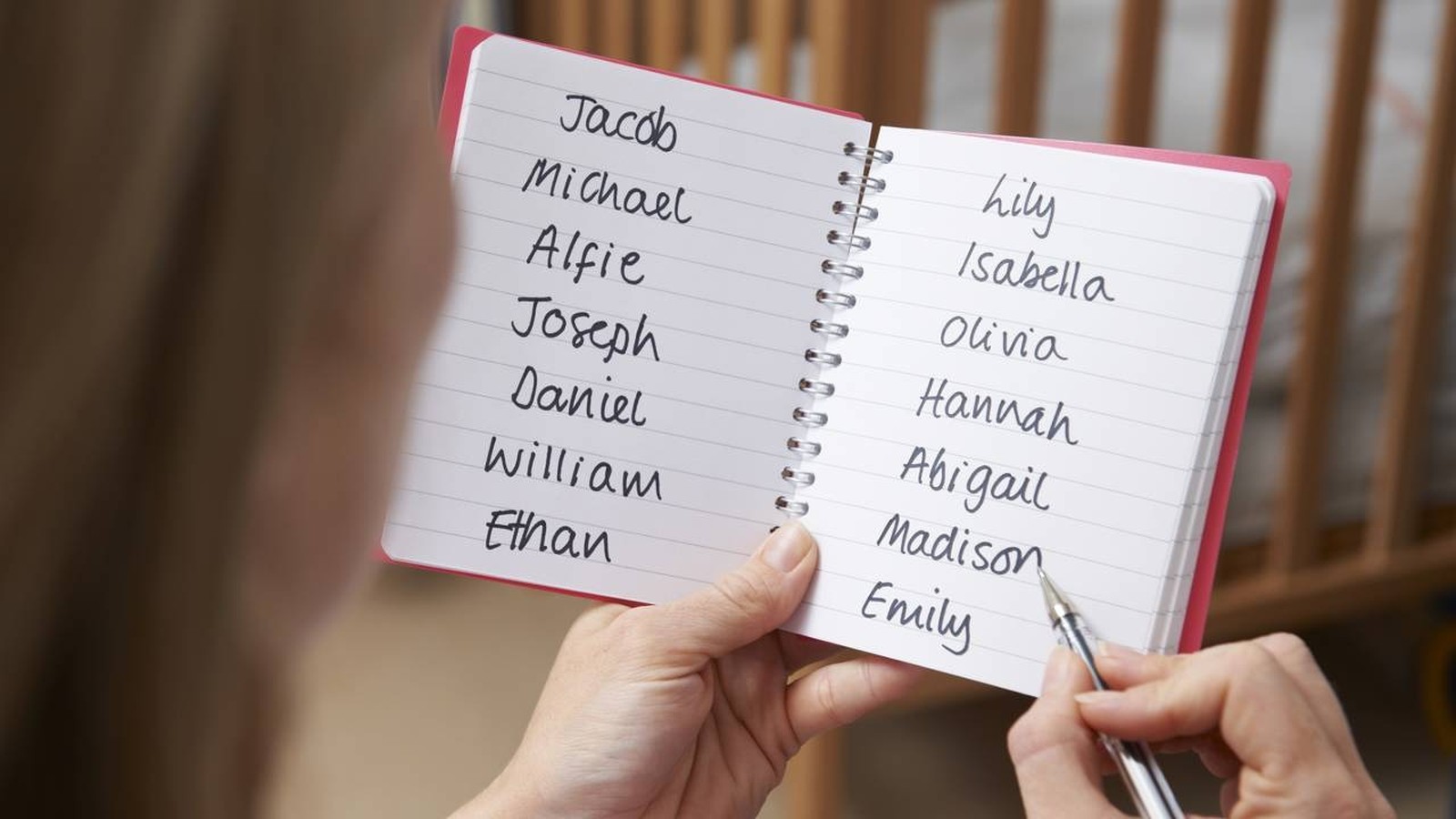 Mão segura caderno com lista de nomes de bebês: Jacob, Michael, Lily, Isabella, Emily