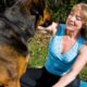 Mulher sorridente acaricia cão grande preto e marrom sentada em tapete azul