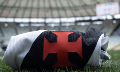Camisa do Vasco da Gama dobrada, com cruz vermelha, sobre a grama de um estádio de futebol