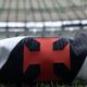 Camisa do Vasco da Gama dobrada, com cruz vermelha, sobre a grama de um estádio de futebol