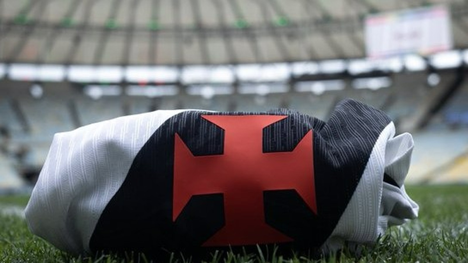 Camisa do Vasco da Gama dobrada, com cruz vermelha, sobre a grama de um estádio de futebol