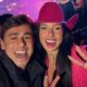 Selfie: Ana Castela sorrindo com homem em evento. Ela usa chapéu rosa e faz sinal