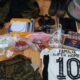 Várias sacolas de drogas, fardamento camuflado, balança, rádios, celular e camisa de time sobre piso