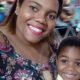 Mulher sorridente e menino em carrossel, com cavalo branco ao fundo