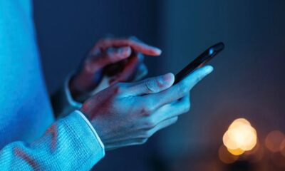 Mãos seguram e interagem com um smartphone em ambiente de pouca luz azul