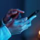 Mãos seguram e interagem com um smartphone em ambiente de pouca luz azul