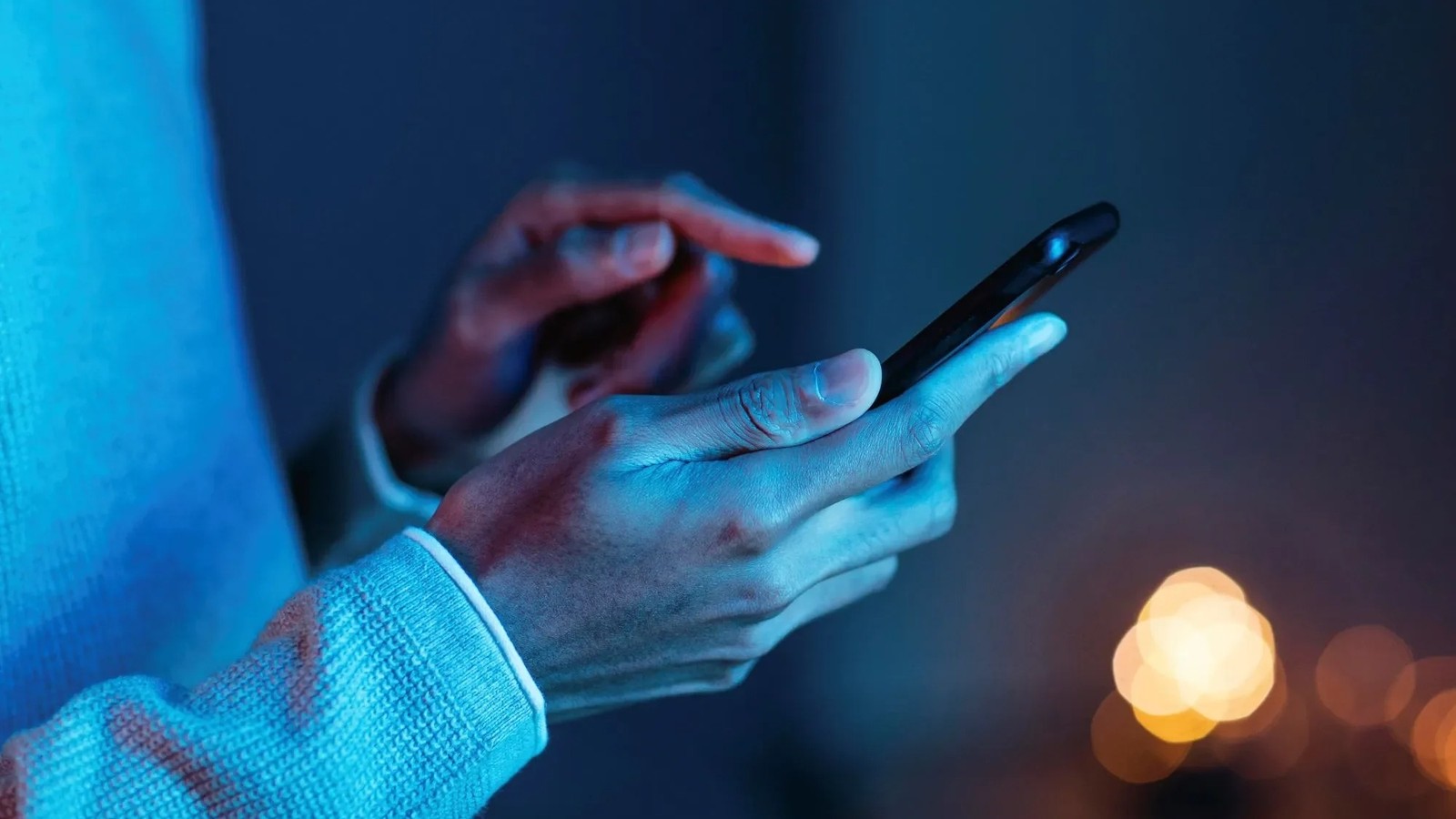 Mãos seguram e interagem com um smartphone em ambiente de pouca luz azul