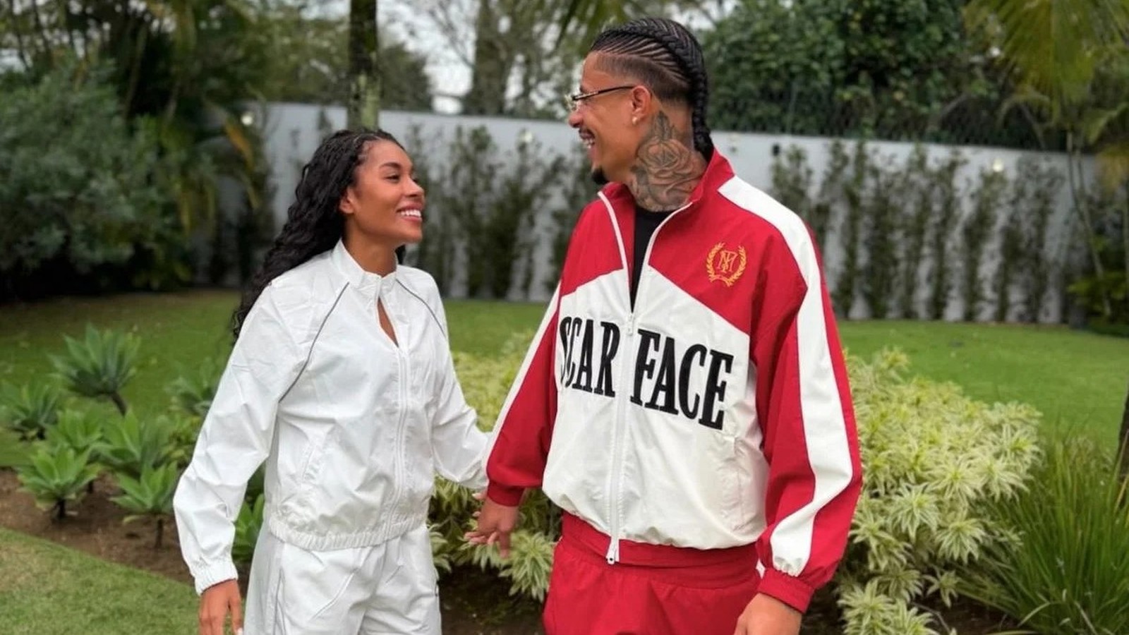 Giovanna Jacobina e Breno Fagundes sorrindo de mãos dadas, ela de branco, ele de agasalho