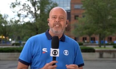 Jornalista Alex Escobar, careca e barbudo, em camisa polo azul segurando microfone da Globo