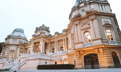 Grande e ornamentado edifício bege com cúpulas, colunas, escadarias brancas e iluminação noturna