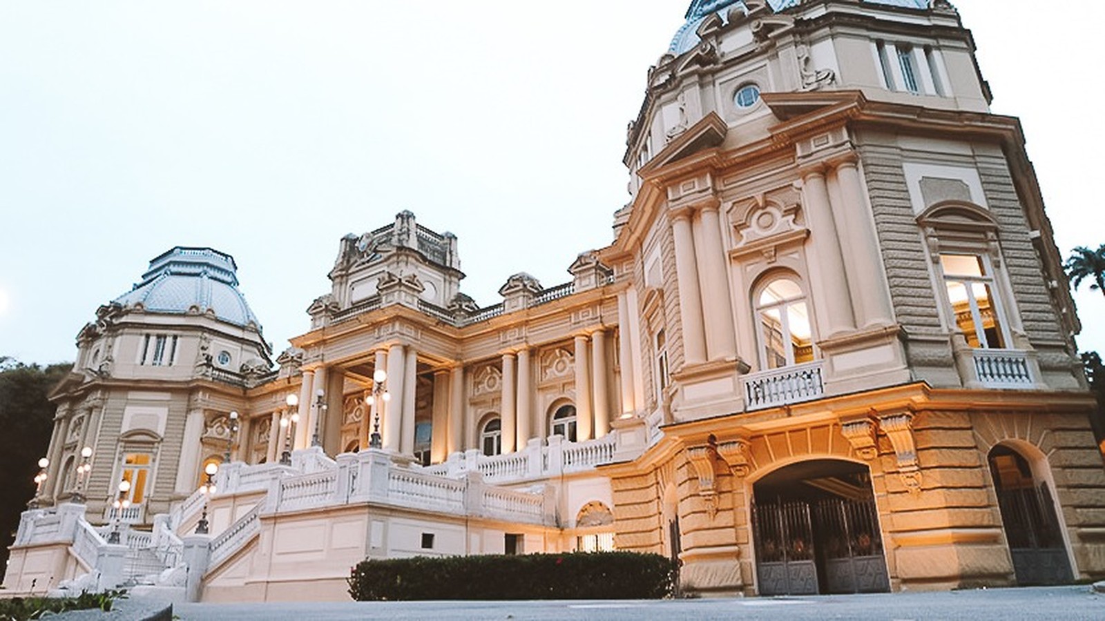 Grande e ornamentado edifício bege com cúpulas, colunas, escadarias brancas e iluminação noturna