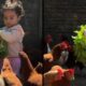 Criança com cabelo cacheado segura alface verde, cercada por galinhas no galinheiro
