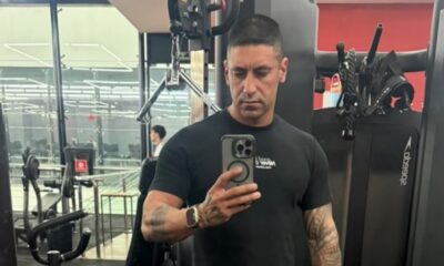 Homem com camiseta preta e tatuagens no braço tirando selfie em uma academia