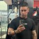 Homem com camiseta preta e tatuagens no braço tirando selfie em uma academia