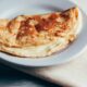 Crepioca dobrada com recheio claro e cremoso em um prato branco, com talheres