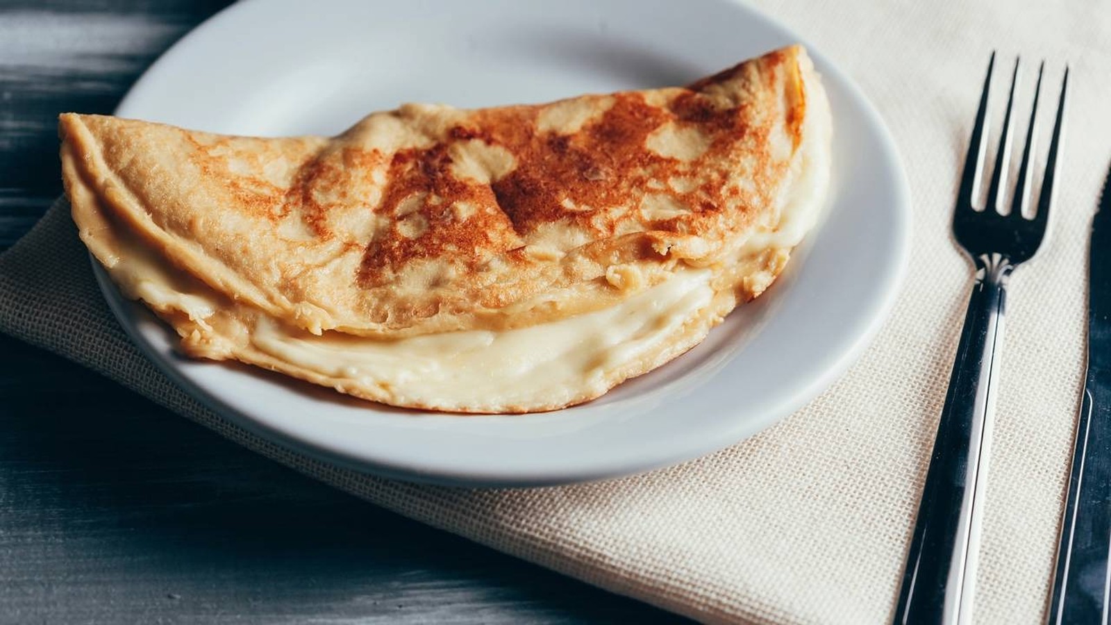 Crepioca dobrada com recheio claro e cremoso em um prato branco, com talheres