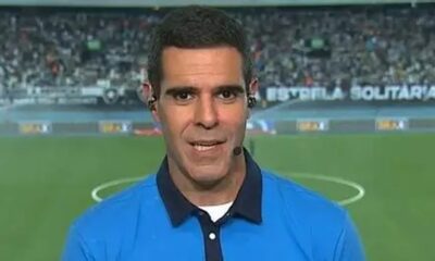 Homem de camisa polo azul e fones, com microfone, em campo de futebol com 'ESTRELA SOLITÁRIA'