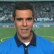 Homem de camisa polo azul e fones, com microfone, em campo de futebol com 'ESTRELA SOLITÁRIA'