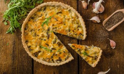 Quiche de alho-poró fatiada em mesa de madeira rústica, com alho e sementes de cominho