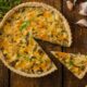 Quiche de alho-poró fatiada em mesa de madeira rústica, com alho e sementes de cominho