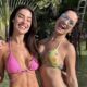Duas mulheres sorridentes de biquíni em jardim tropical com palmeiras e gramado verde