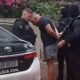 Homem algemado por três policiais ao lado de viatura Polícia Civil, placa LUF8E23