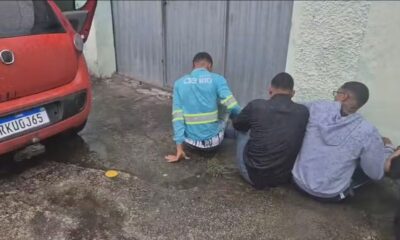 Três homens sentados, um de uniforme azul, junto a carro vermelho placa RKUGJ65