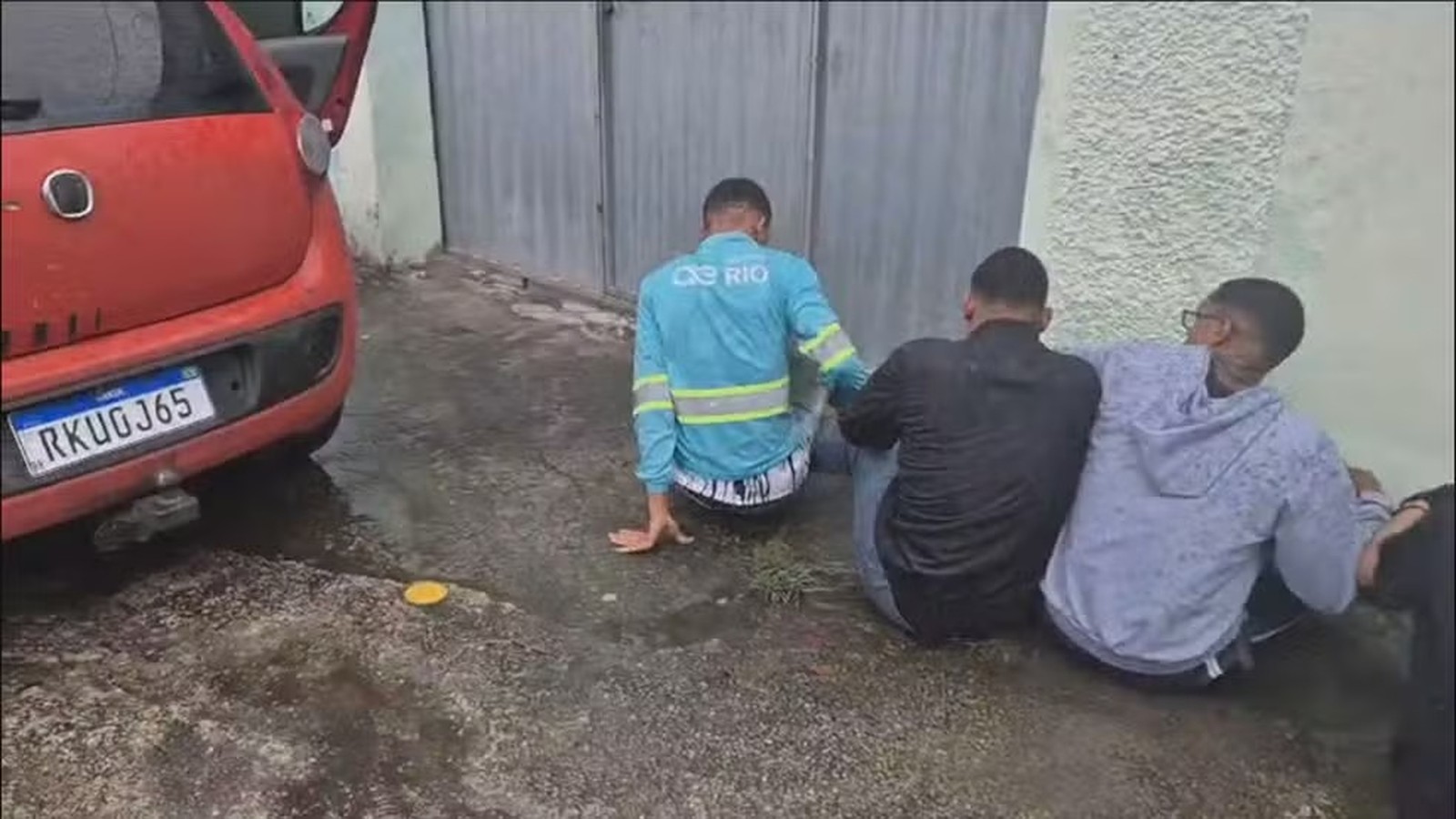 Três homens sentados, um de uniforme azul, junto a carro vermelho placa RKUGJ65