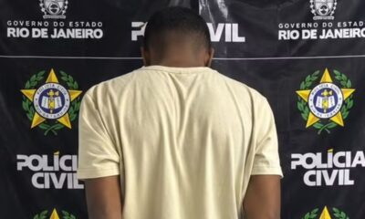 Homem de costas em camiseta clara, em frente a banner da Polícia Civil