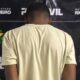 Homem de costas em camiseta clara, em frente a banner da Polícia Civil