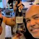 Dois homens sorridentes, um com barba e outro careca, brindam com vinho tinto e garrafa Barca-Velha 2004