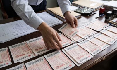 Mãos de pessoa organizam pilhas de bilhetes de loteria chinesa em mesa de madeira com documentos