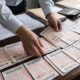 Mãos de pessoa organizam pilhas de bilhetes de loteria chinesa em mesa de madeira com documentos