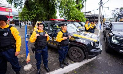 Agentes da Força Municipal com uniformes e viaturas pretas e amarelas estacionadas na rua