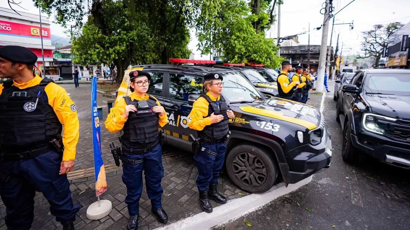 Agentes da Força Municipal com uniformes e viaturas pretas e amarelas estacionadas na rua