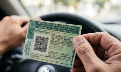 Mãos de motorista segurando a Carteira Nacional de Habilitação verde dentro de um carro