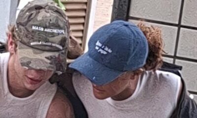 Duas pessoas de boné. Um camuflado com 'MASS ARCRETOL', outro azul
