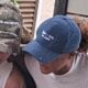 Duas pessoas de boné. Um camuflado com 'MASS ARCRETOL', outro azul