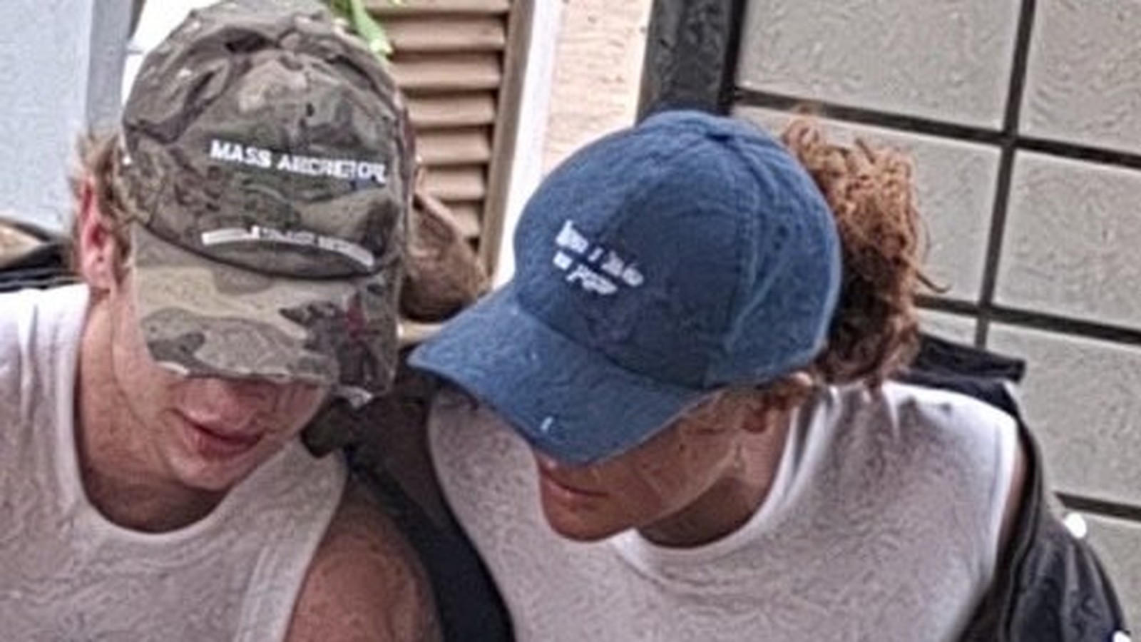 Duas pessoas de boné. Um camuflado com 'MASS ARCRETOL', outro azul