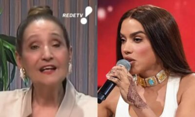 Mulher mais velha à esquerda falando, mulher jovem à direita segurando microfone com henna e colar