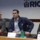 Três homens em coletiva de imprensa, com Victor Santos à direita e uma bola de futebol americano na mesa