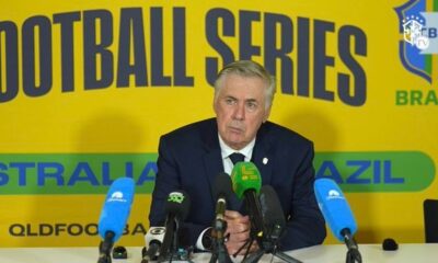Carlo Ancelotti, terno azul, microfones, fundo amarelo com "FOOTBALL SERIES AUSTRALIA BRAZIL CBF TV"
