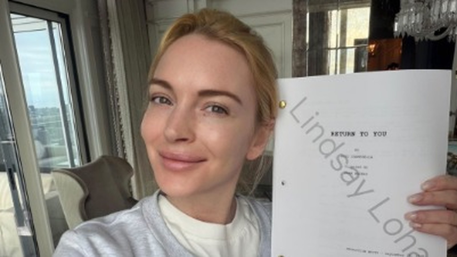 Lindsay Lohan sorrindo, segurando roteiro "Return to You" com seu nome em marca d'água.