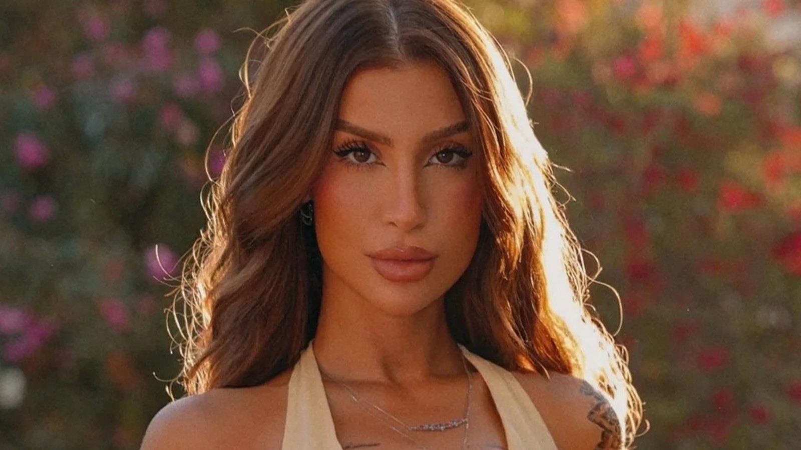 Close-up de Bianca Andrade com cabelo castanho ondulado, maquiagem e colar, olhando fixamente