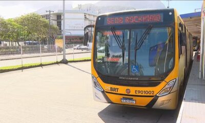 Ônibus amarelo BRT com letreiro "ROCKINRIO" e símbolo de acessibilidade parado em terminal