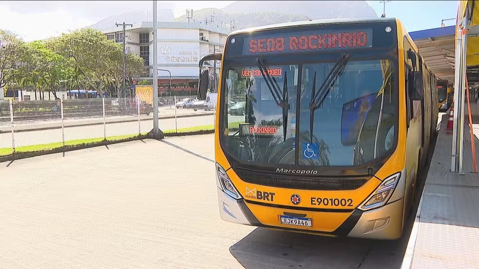 Ônibus amarelo BRT com letreiro "ROCKINRIO" e símbolo de acessibilidade parado em terminal