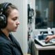 Mulher jovem com fones de ouvido pretos faz exame de audiometria em cabine à prova de som